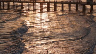 Symbolbild: Eine Luftaufnahme zeigt Menschen auf dem Pier von Huntington Beach über dem Pazifik, während eine Person im Wasser watet (Aufnahme vom 1. Juli 2026 in Huntington Beach, Kalifornien).