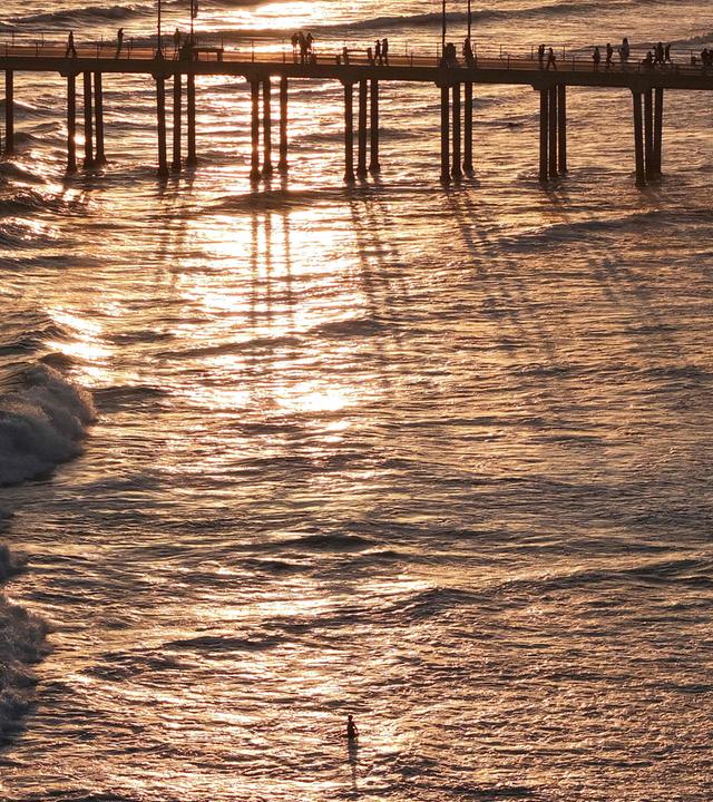 Symbolbild: Eine Luftaufnahme zeigt Menschen auf dem Pier von Huntington Beach über dem Pazifik, während eine Person im Wasser watet (Aufnahme vom 1. Juli 2026 in Huntington Beach, Kalifornien).