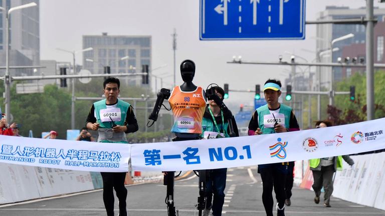 Robotic participant "Tiangong Ultra" (C) competes as engineers run alongside during the Beijing E-Town half-marathon and humanoid robots half-marathon in the Beijing Economic-Technological Development Area in southeast Beijing, China, April 19, 2025.