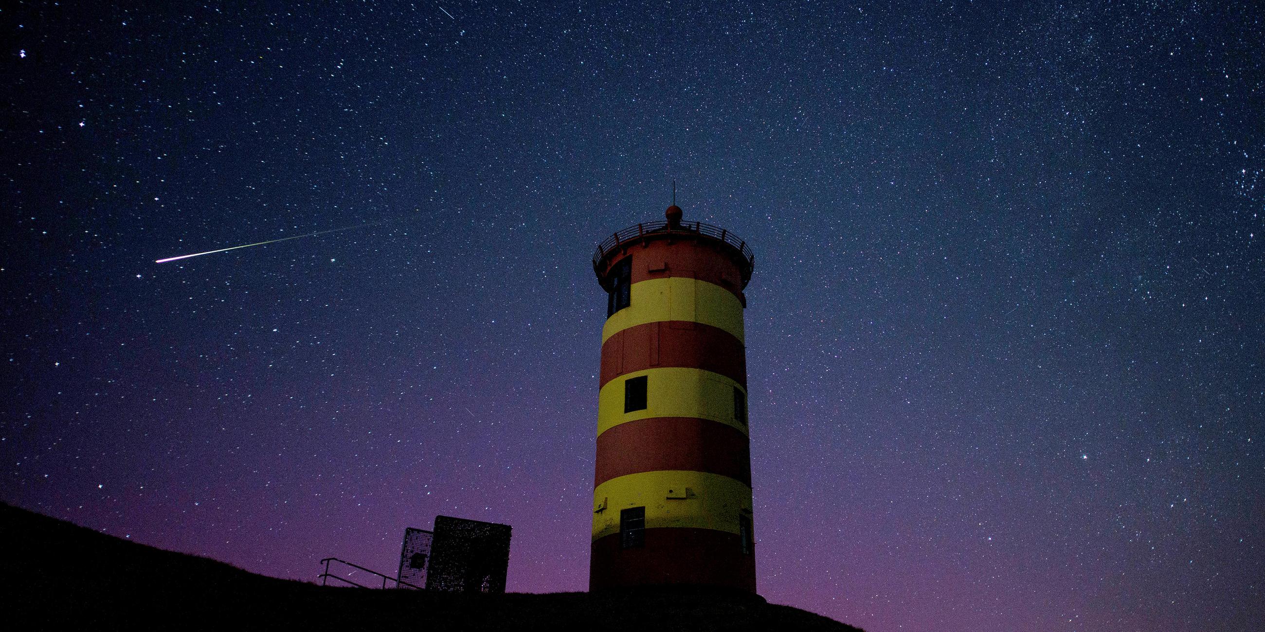 Eine Sternschnuppe leuchtet über der Nordsee am Nachthimmel über dem Pilsumer Leuchtturm