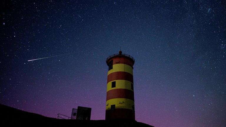 Eine Sternschnuppe leuchtet über der Nordsee am Nachthimmel über dem Pilsumer Leuchtturm