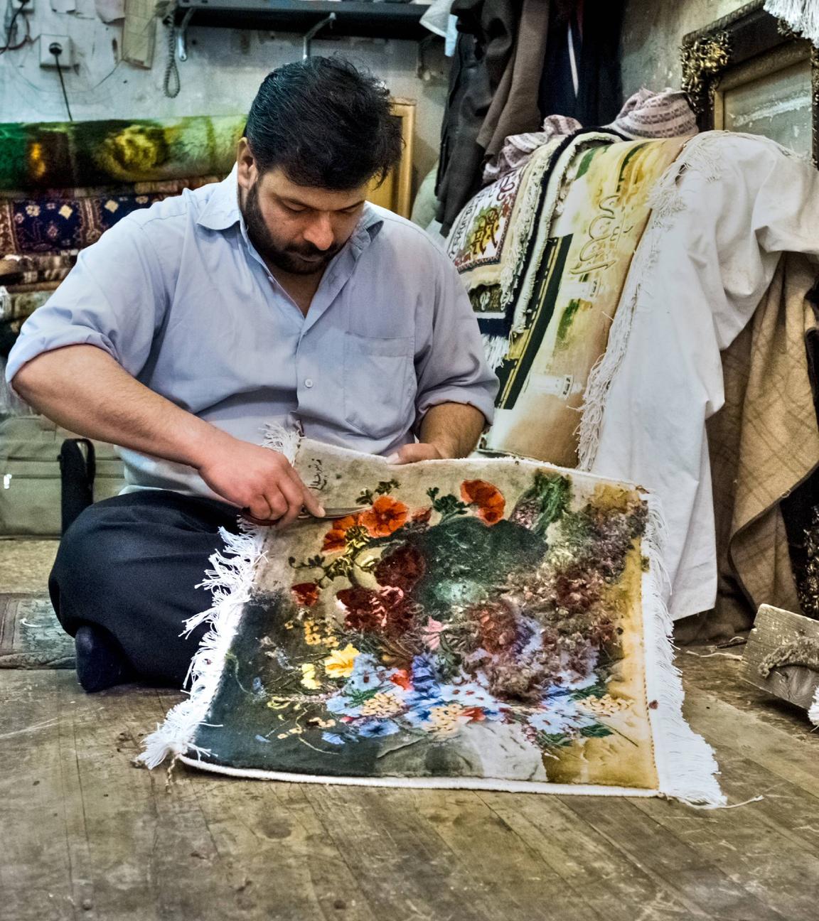 Ein Mann knüpft in seiner Werkstatt an einem Teppich
