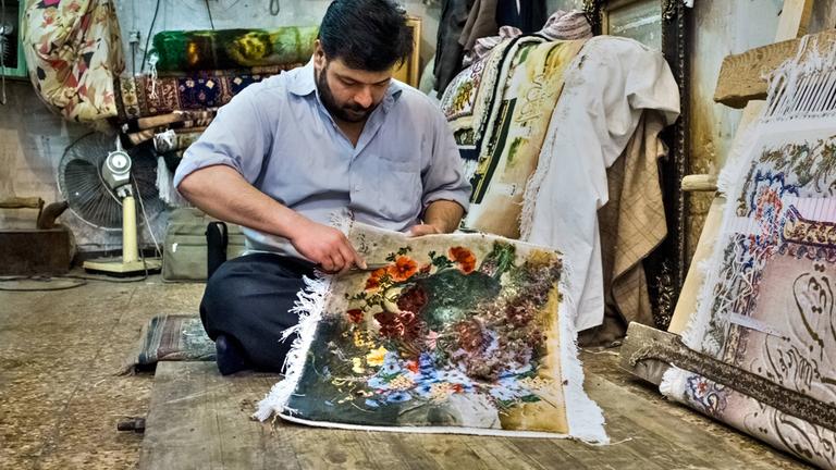 Ein Mann knüpft in seiner Werkstatt an einem Teppich