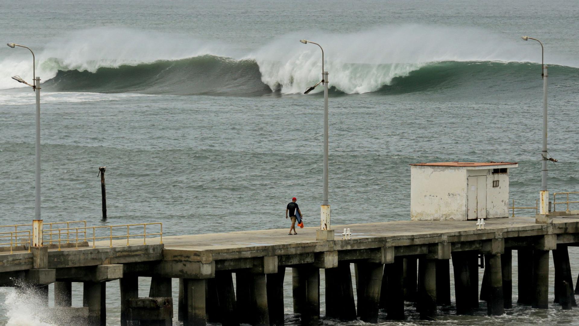 Ein Mann geht auf einem Dock, während in Lobitos, Provinz Talara, Peru, Flutwellen zu sehen sind
