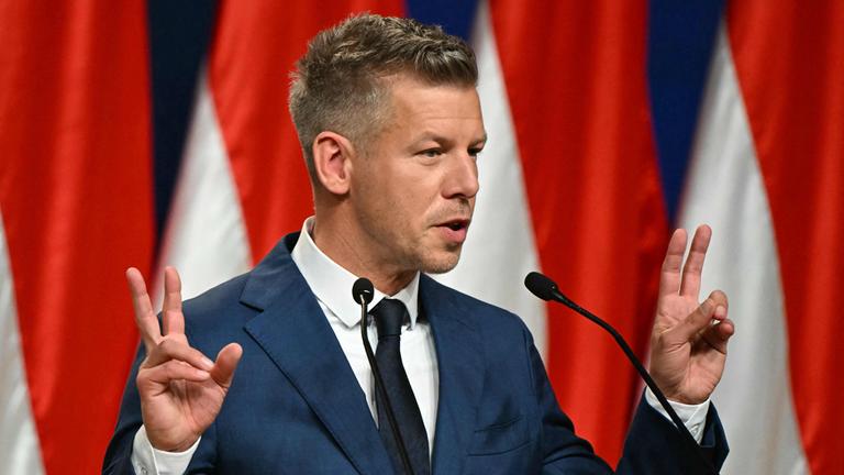 Peter Magyar bei einer Pressekonferenz, gestikuliert und hält beide Hände ähnlich des Victory-Zeichens neben sich hoch.