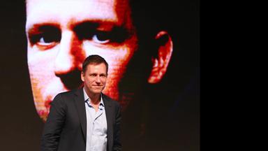 Ein Mann läuft vor einem riesigen an die Wand projizierten Fotos seines eigenen Gesichts.
