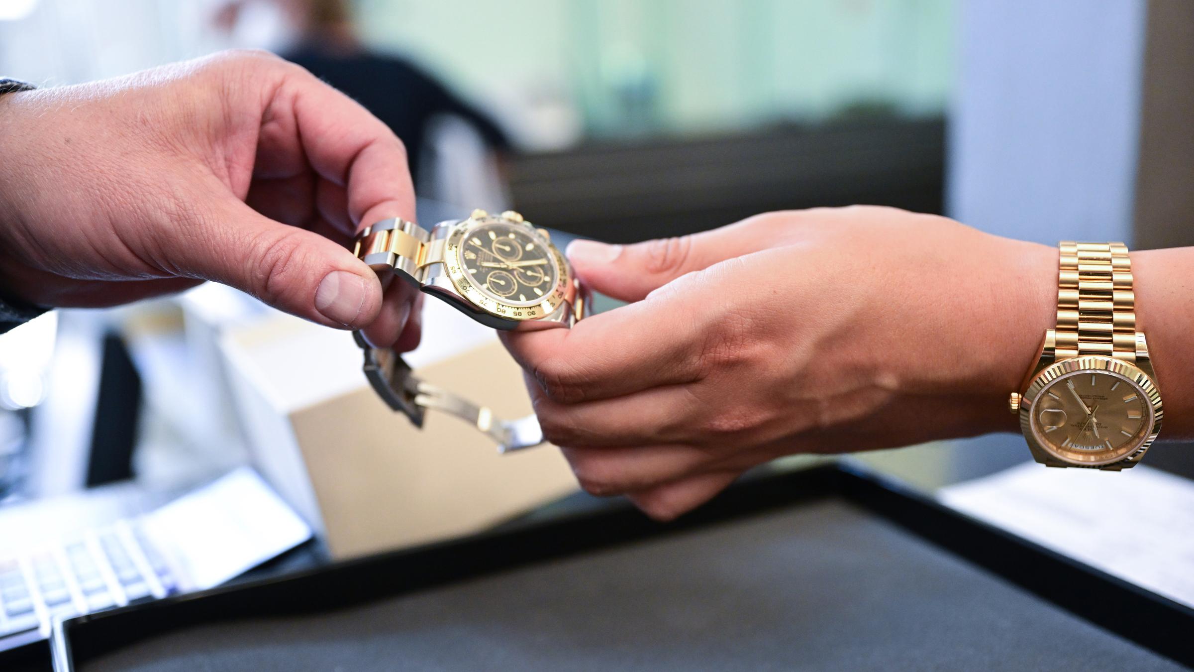 Eine Luxusuhr wird in einem Pfandleihhaus von einer Hand in die andere gegeben.