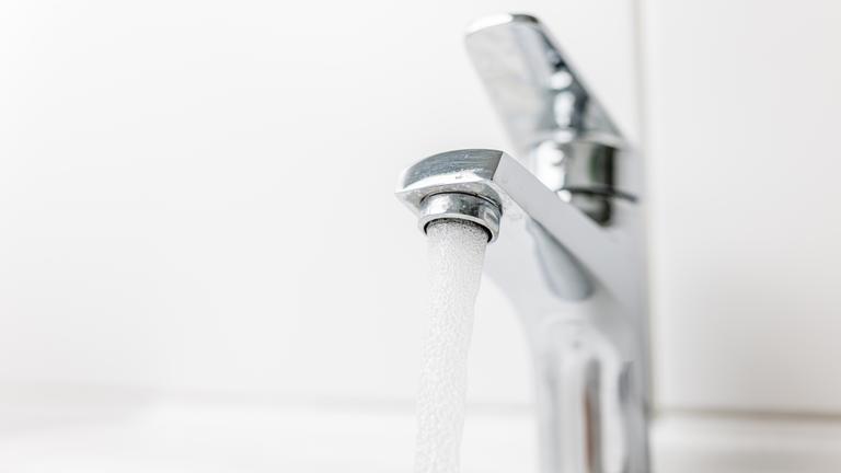 Ein Wasserhahn auf einem weißen Waschbecken mit Fließen im Hintergrund