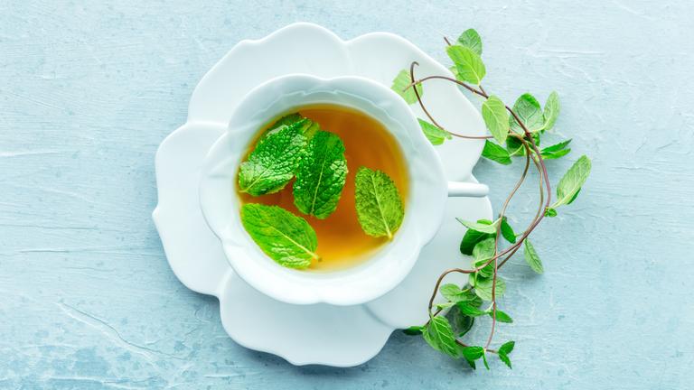 Eine Tasse Pfefferminztee mit frischen Minzblättern, über Kopf