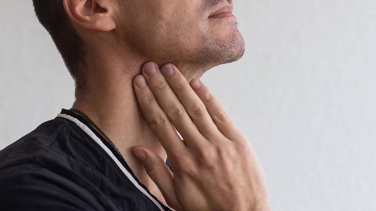Ein Mann greift sich an den Hals.