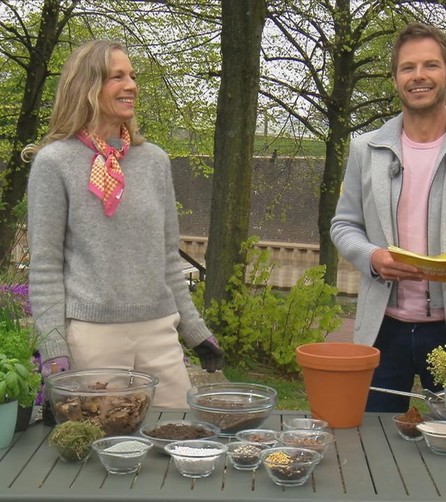 Anja Koenzen und Florian Weiss stehen vor einem Tisch mit Blumentöpfen und Erde