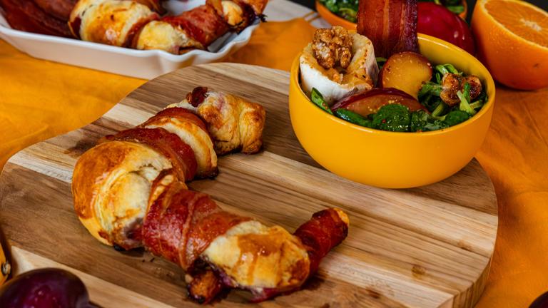 Ein Pflaumenhörnchen mit Speck neben einer Schüssel auf einem Brettchen