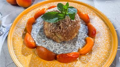 Pflaumenknödel mit glasierten Aprikosen auf einem orangenen Dessertteller.