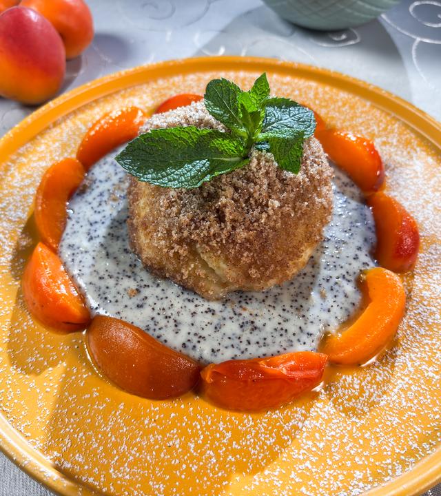 Pflaumenknödel mit glasierten Aprikosen auf einem orangenen Dessertteller.