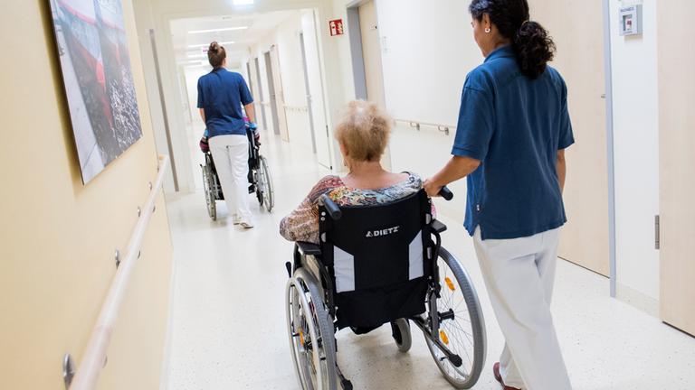 Archiv: Zwei Pflegerinnen schieben in einem Klinikum Patienten mit Rollstühlen durch einen Flur