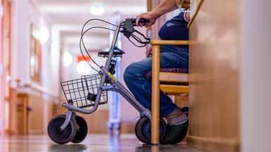 Symbolbild:  Ein Bewohner sitzt mit seinem Rollator auf einem Flur in einem Pflegeheim.