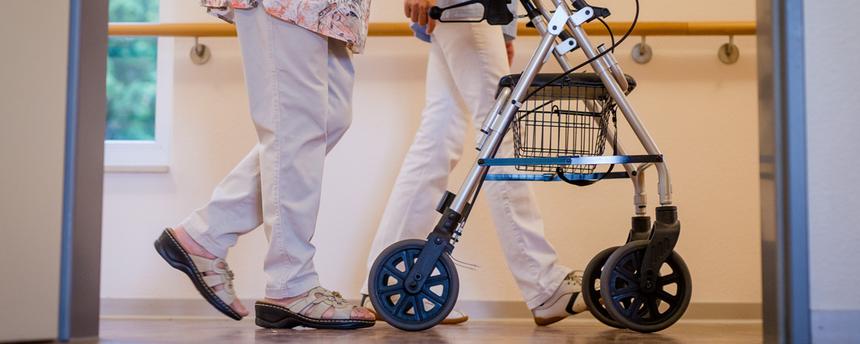 Symbolbild:  Eine Pflegekraft geht in einem Pflegeheim mit einer älteren Dame über einen Korridor. 