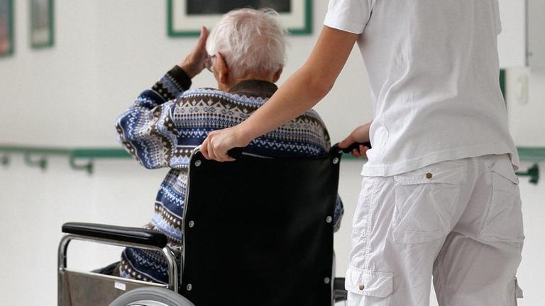 Pflegerin schiebt eine alte Frau im Rollstuhl