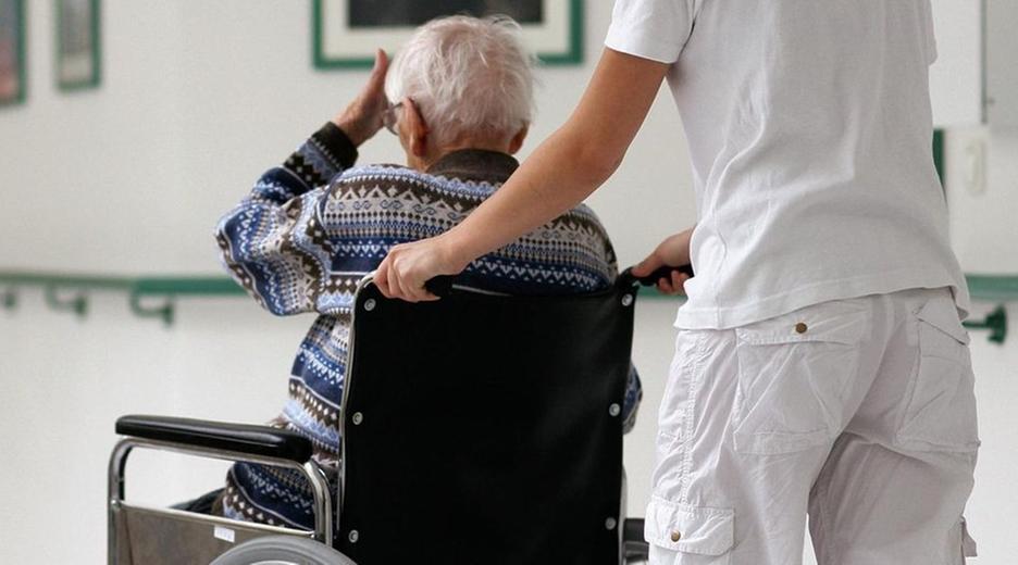 Pflegerin schiebt eine alte Frau im Rollstuhl
