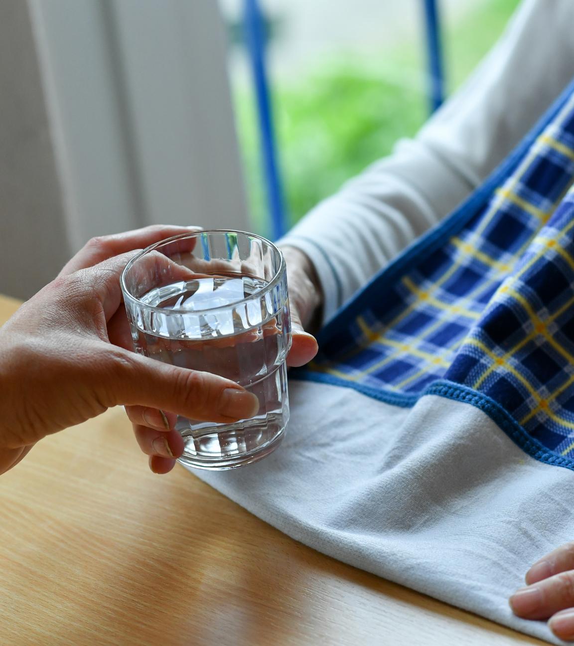 Einer pflegebedürftigen Person wird ein Glas Wasser gereicht.