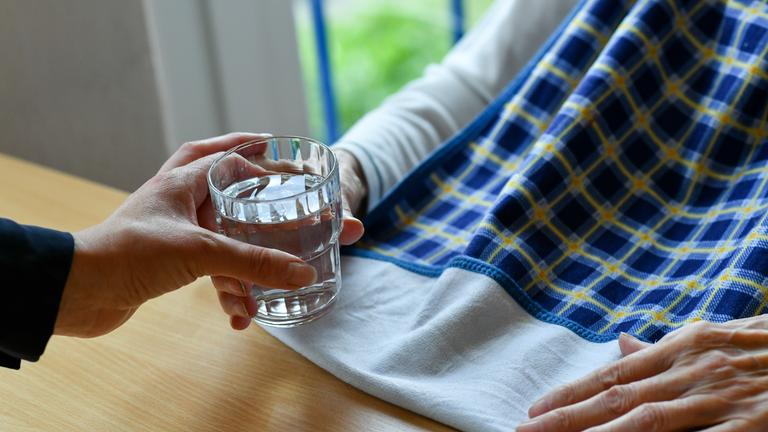 Einer pflegebedürftigen Person wird ein Glas Wasser gereicht.