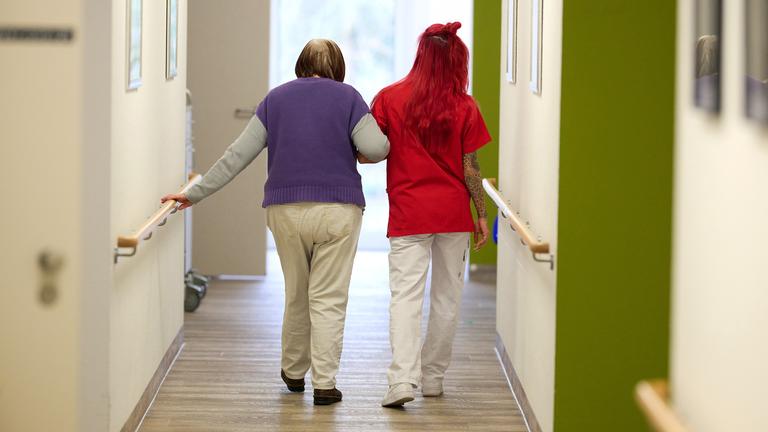 Eine Pflegerin begleitet eine Pflegebedürftige durch einen Hausflur.