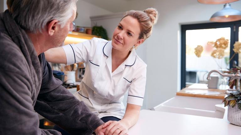 Pflegekraft berührt Pflegebedürftigen an der Schulter.