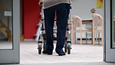 Ein Bewohner eines Pflegezentrums geht mit dem Rollator durchs Haus.