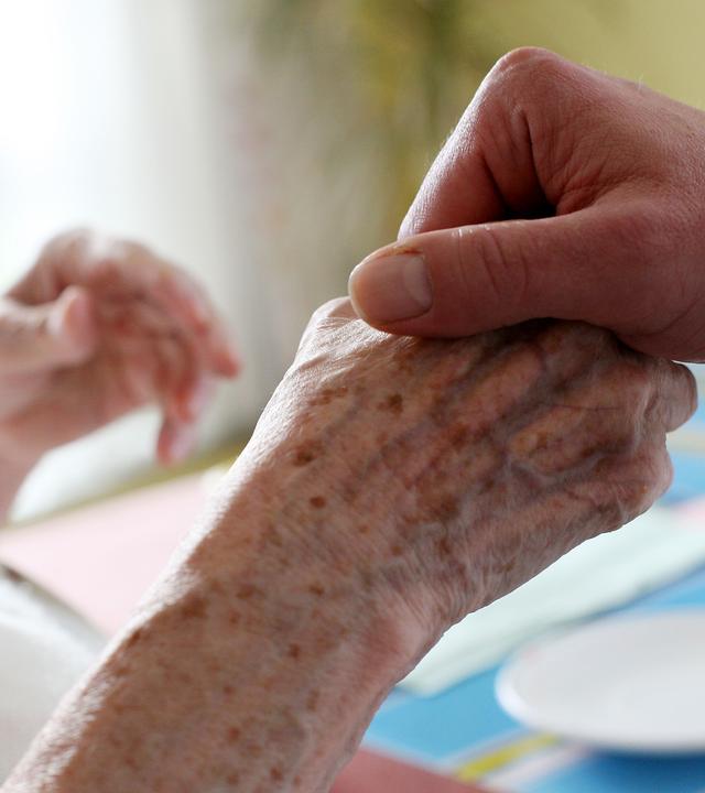 Ein Mitarbeiter eines Alten-und Pflegeheims hält die Hand einer Bewohnerin