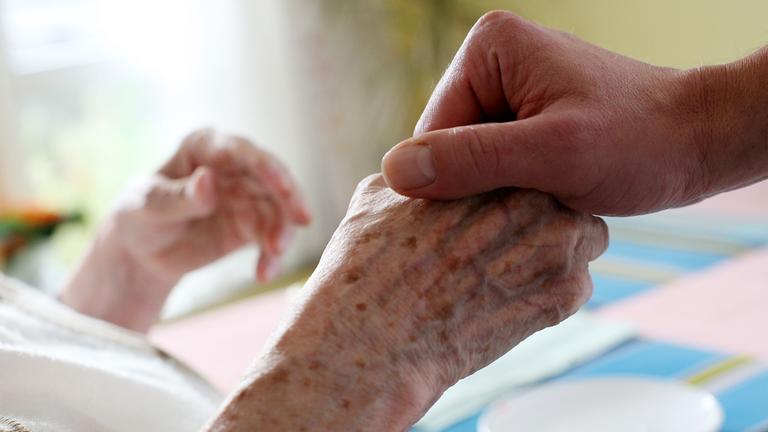 Ein Mitarbeiter eines Alten-und Pflegeheims hält die Hand einer Bewohnerin