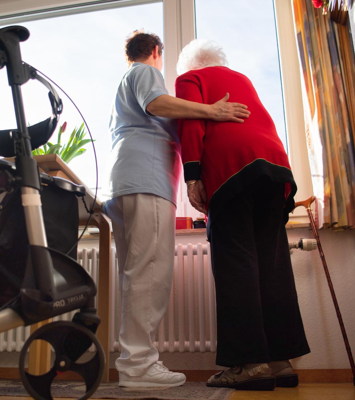 Baden-Württemberg, Böblingen: Eine Pflegerin (l) und eine Bewohnerin des Pflegeheims schauen zusammen aus einem Fenster im Wohnbereich des Pflegeheims.