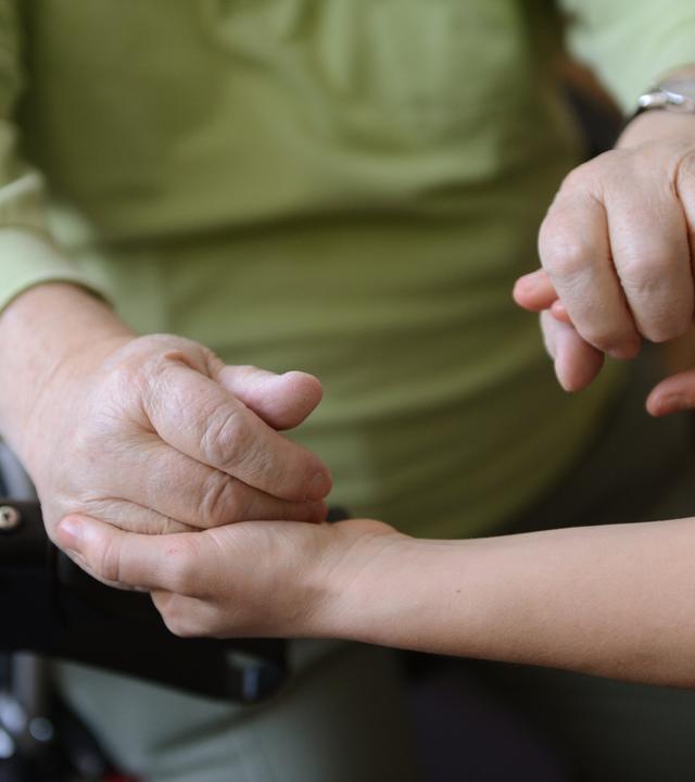 Eine junge Frau hält die Hände eines alten Mannes
