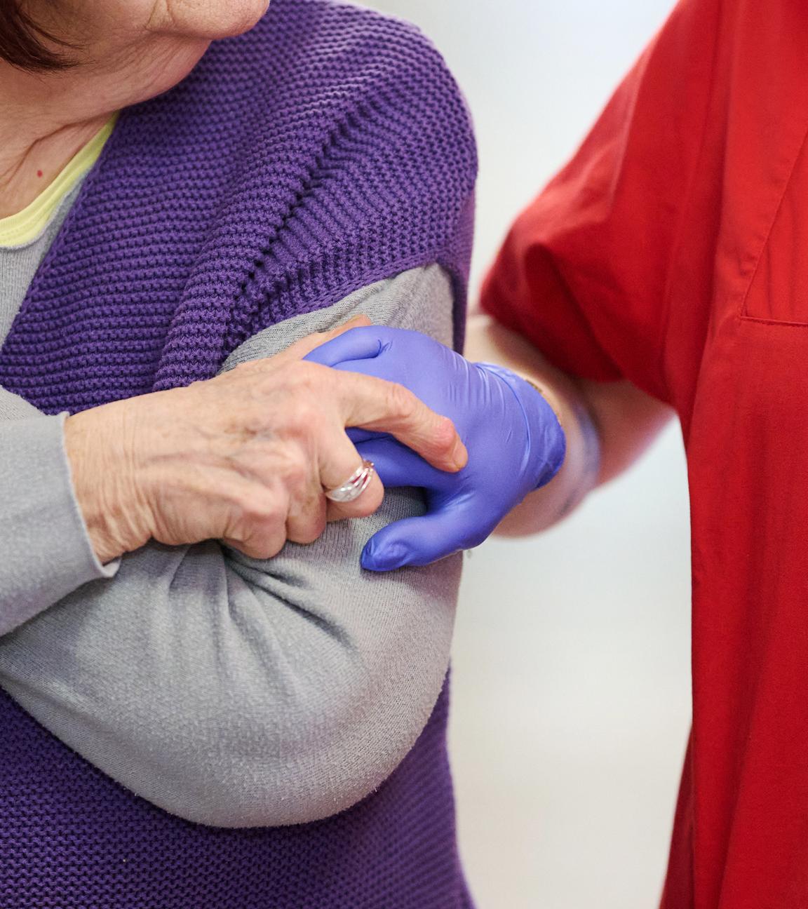 Pflegekraft nimmt Bewohnerin an der Hand.