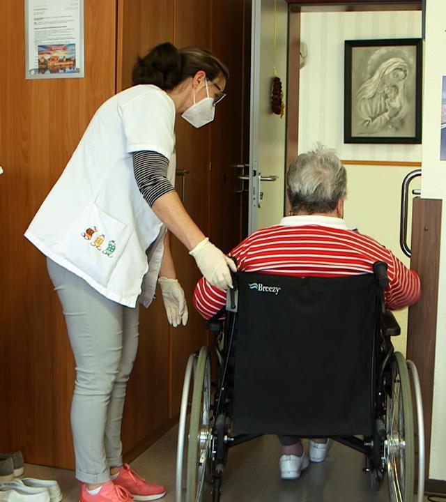 Pflegerin hilft Bewohnerin im Rollstuhl