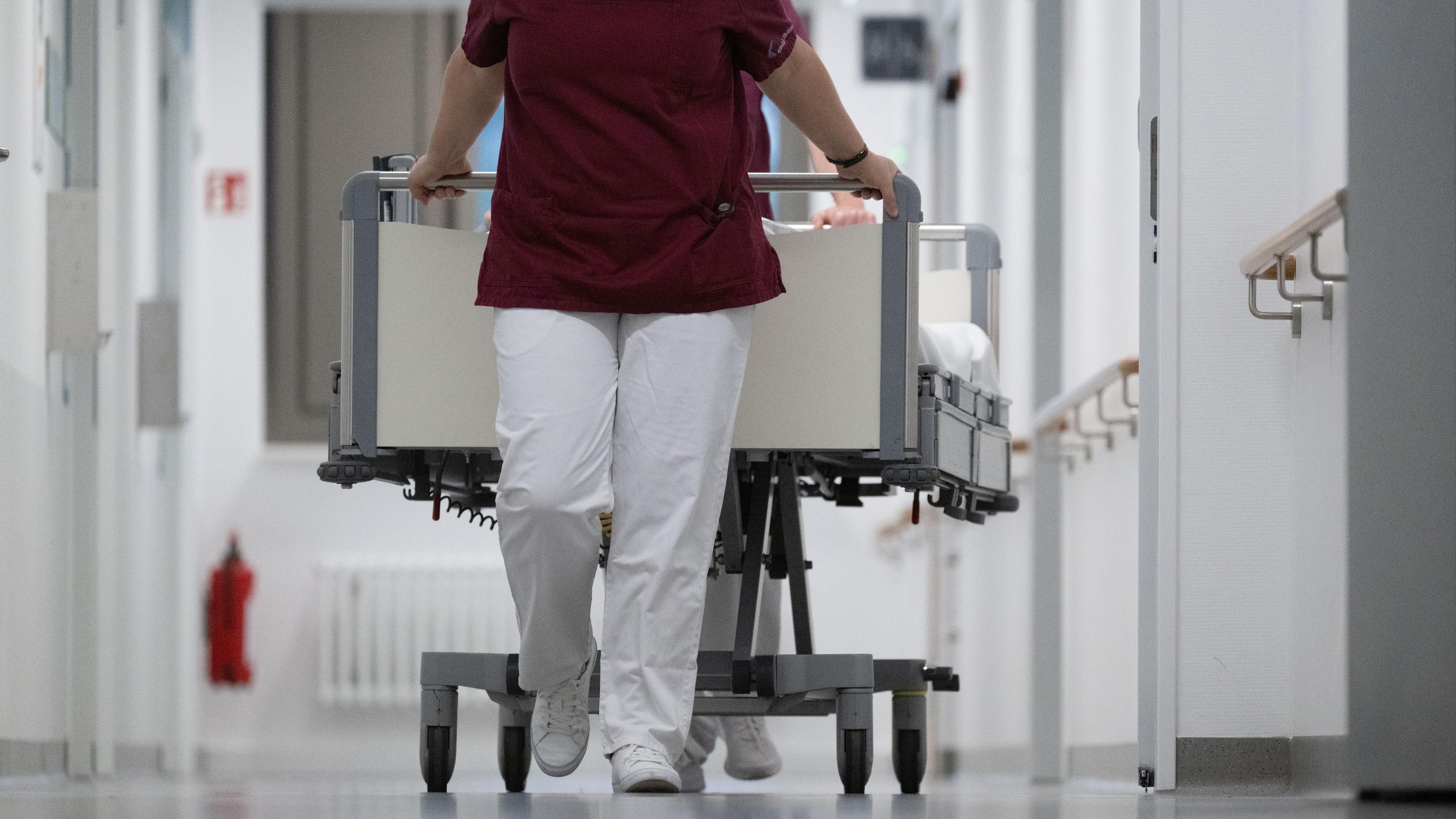 15.05.2024, Baden-Württemberg, Stuttgart: Eine Krankenpflegerin und ein Krankenpfleger schieben ein Krankenbett durch den Gang einer Station eines Krankenhauses.