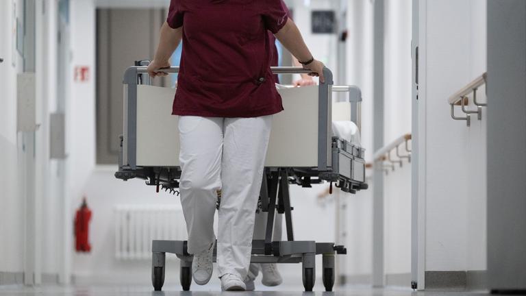 15.05.2024, Baden-Württemberg, Stuttgart: Eine Krankenpflegerin und ein Krankenpfleger schieben ein Krankenbett durch den Gang einer Station eines Krankenhauses.