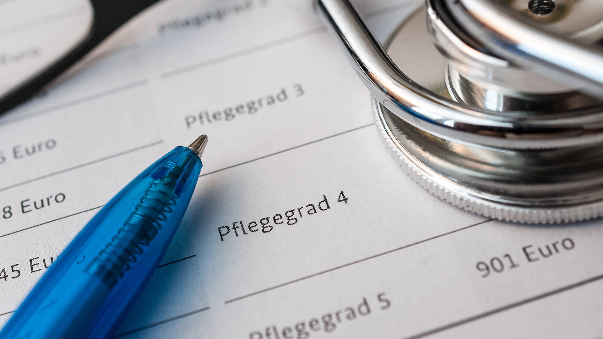 Formulare zur Beantragung eines Pflegegrads, darauf liegen ein Kugelschreiber, eine Brille und ein Stethoskop.