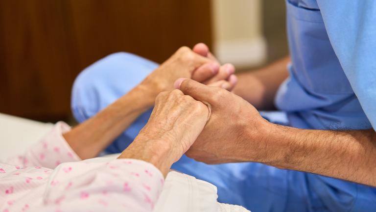 Eine Pflegekraft hält die Hände einer Frau.