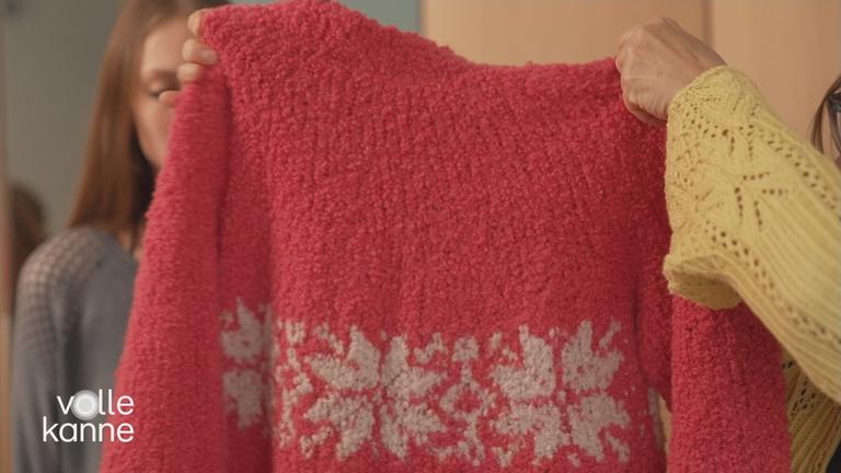 Ein roter Wollpulli wird ins Bild gehalten.