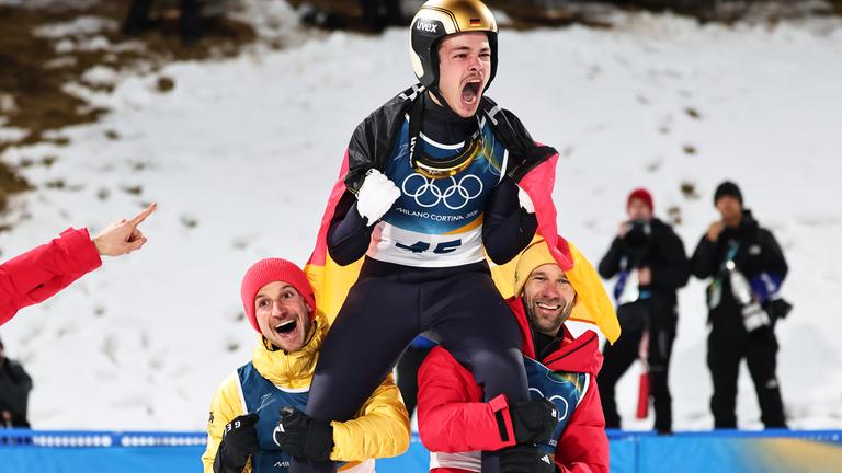 Philipp Raimund (GER) jubelt mit seinen Teamkollegen Felix Hoffmann (GER) und Pius Paschke (GER) nach seinem Sieg auf der Normalschanze, Durchgang 2, Olympische Winterspiele 2026.
