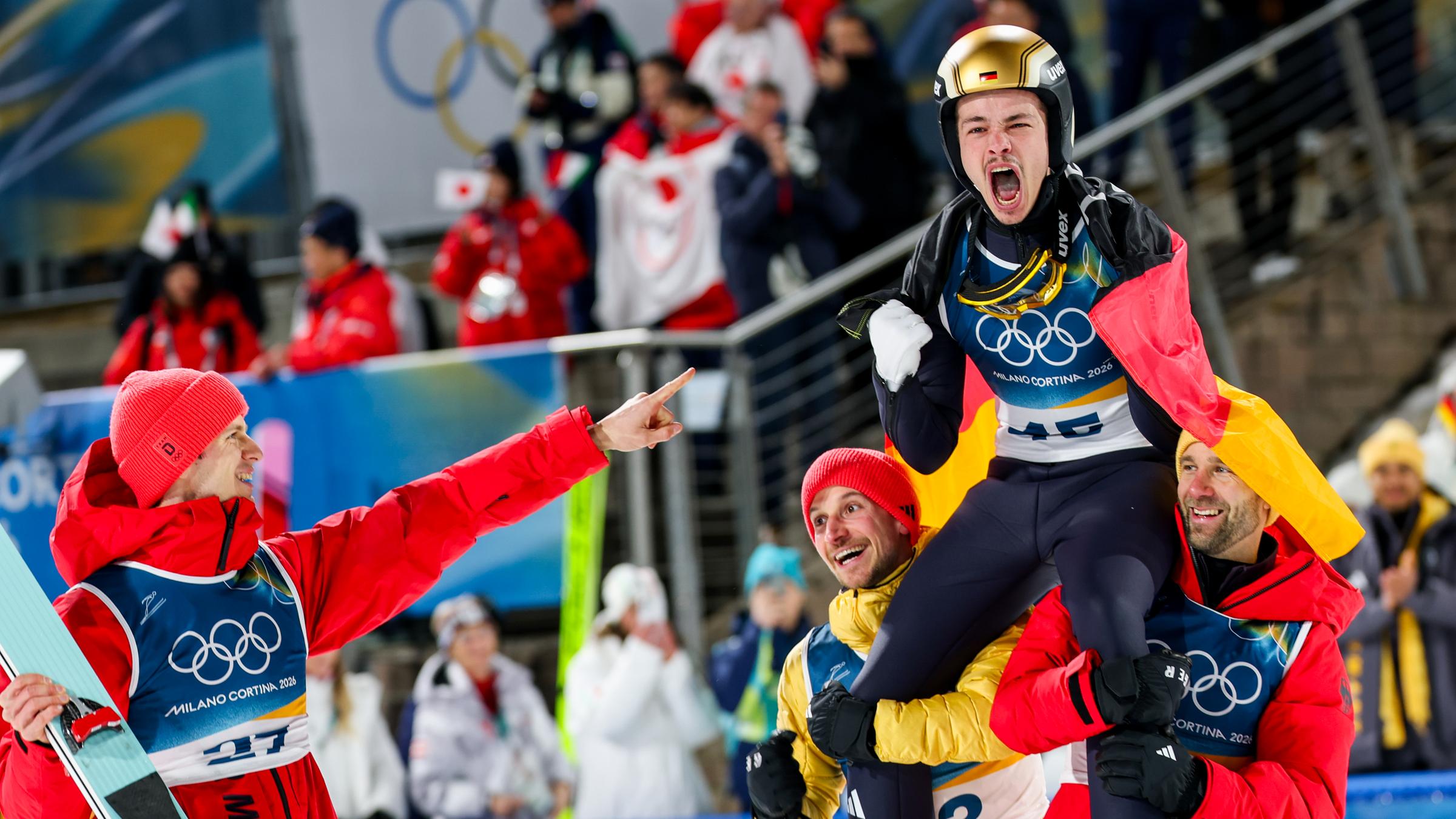 Philipp Raimund jubelt über seinen Sieg mit Andreas Wellinger und Felix Hoffmann auf der Normalschanze bei den Olympischen Winterspielen Milano Cortina 2026.