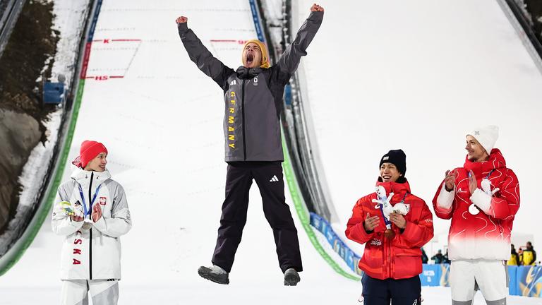 Olympiasieger Philipp Raimund (GER) jubelt bei der Siegerehrung auf der Normalschanze neben Kacper Tomasiak (POL), Ren Nikaido (JPN) und Gregor Deschwanden (SUI) über seine Goldmedaille.