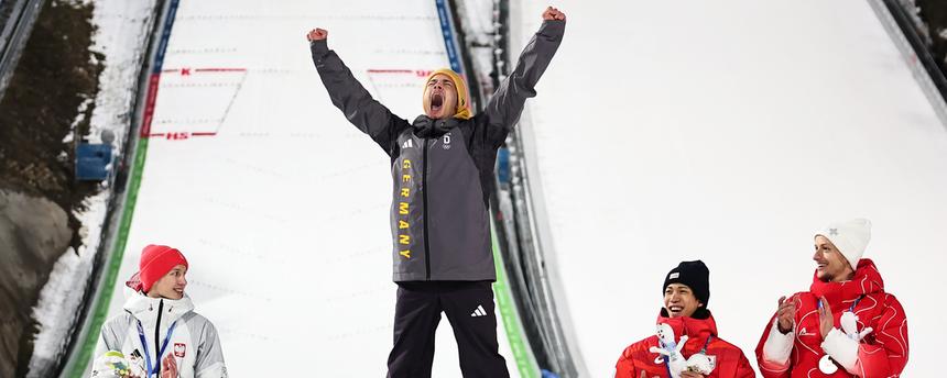 Olympiasieger Philipp Raimund (GER) jubelt bei der Siegerehrung auf der Normalschanze neben Kacper Tomasiak (POL), Ren Nikaido (JPN) und Gregor Deschwanden (SUI) über seine Goldmedaille.