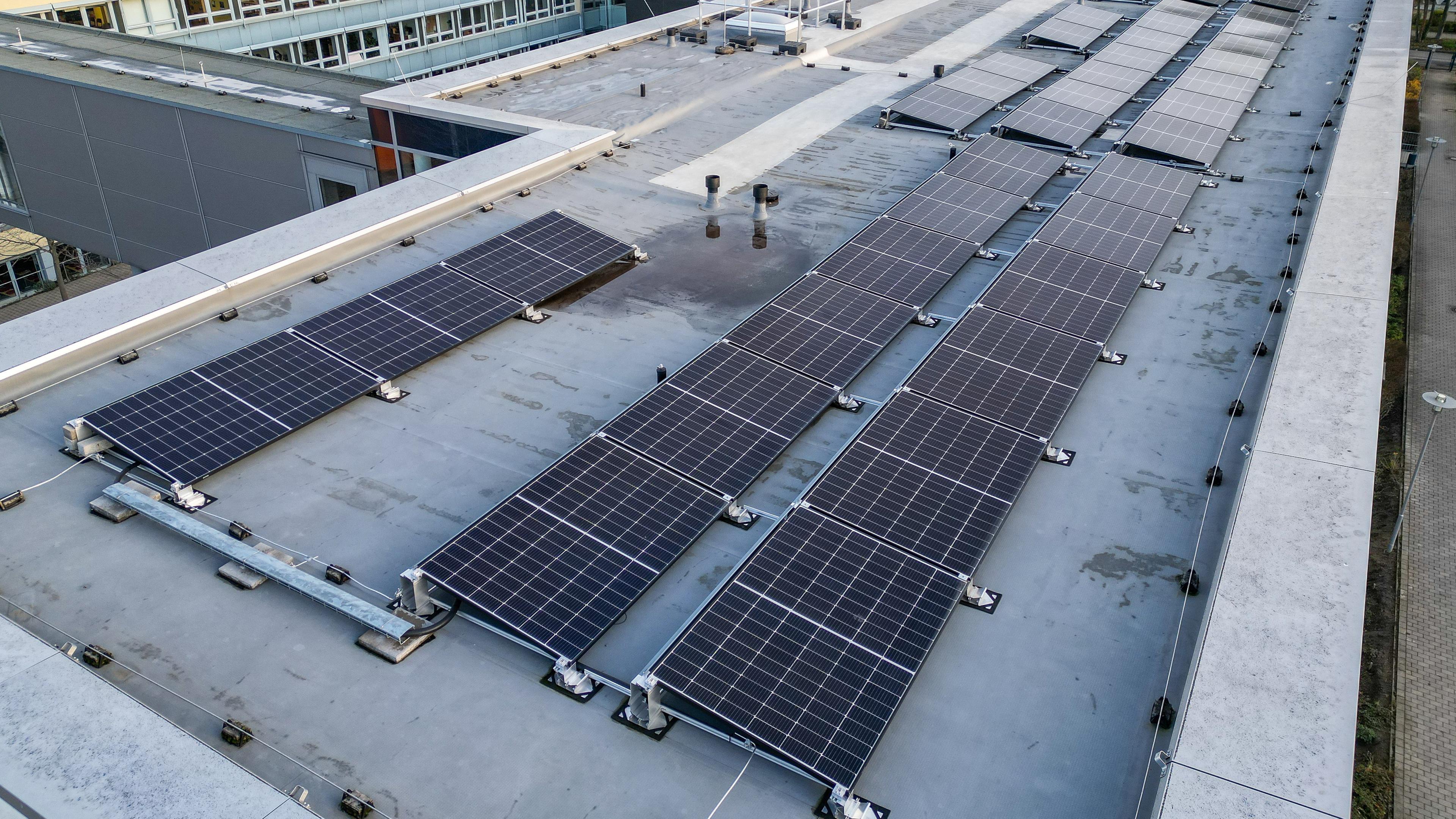 Mehrere Solaranlagen auf dem Flachdach eines Gebäudekomplexes.