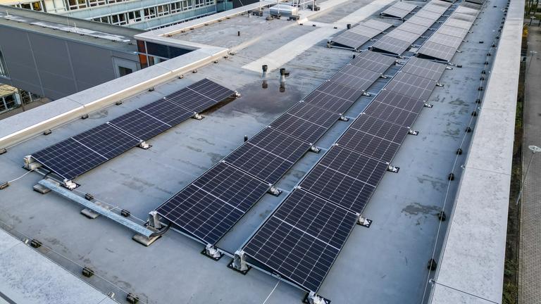 Mehrere Solaranlagen auf dem Flachdach eines Gebäudekomplexes.