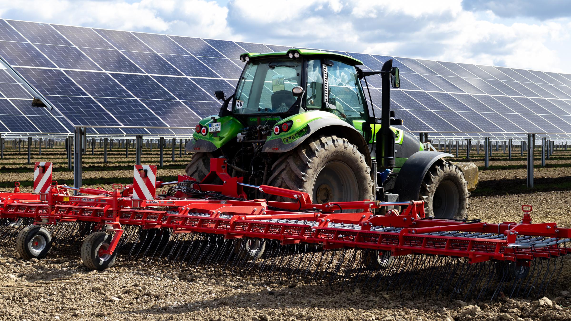 Ein Traktor wird auf einem Feld eingesetzt, dahinter stehen Solarzellen.
