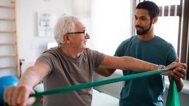 Ein älterer Mann trainiert mit einem Physiotherapeuten.