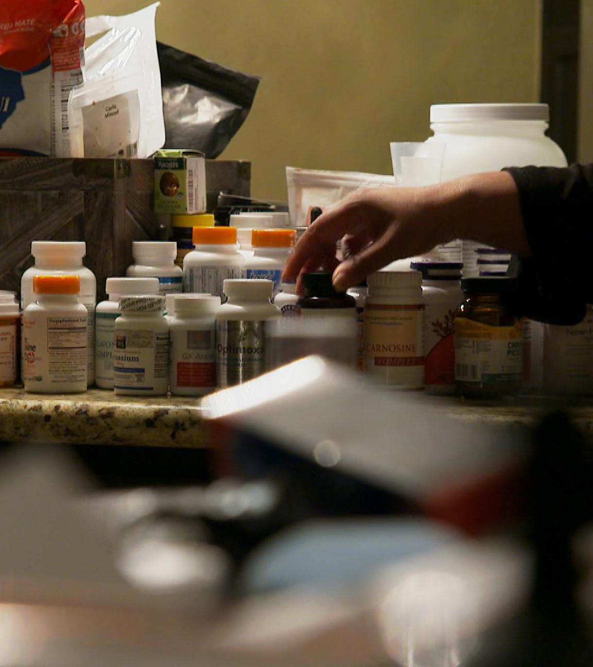 "Pillen, Pulver, Wunderheiler - Das Geschäft mit der Alternativmedizin": Auf einem Tisch stehen zahlreiche Pillendosen. Eine Person, von der nur die Arme zu sehen sind, greift nach einer der Dosen.