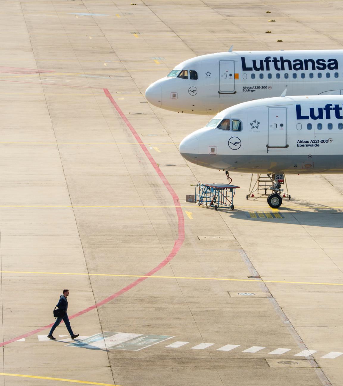 30.09.2025, Hessen, Frankfurt/Main: Ein Mann geht an zwei Lufthansamaschinen vorbei, die auf einer Freifläche vor einer Wartungshalle stehen. 