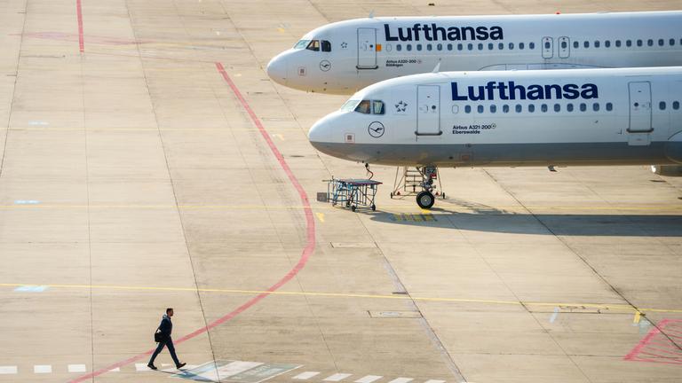 30.09.2025, Hessen, Frankfurt/Main: Ein Mann geht an zwei Lufthansamaschinen vorbei, die auf einer Freifläche vor einer Wartungshalle stehen. 